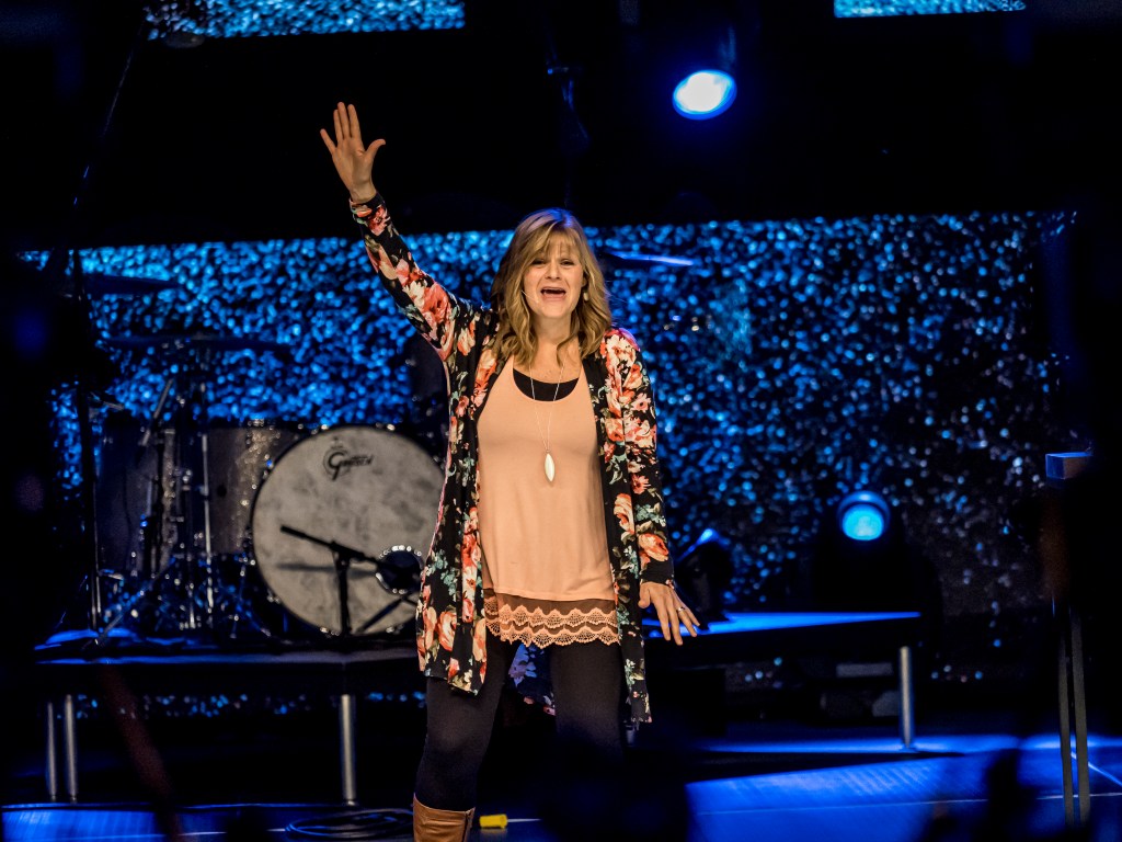 Lisa on stage at a church holding her hand up
